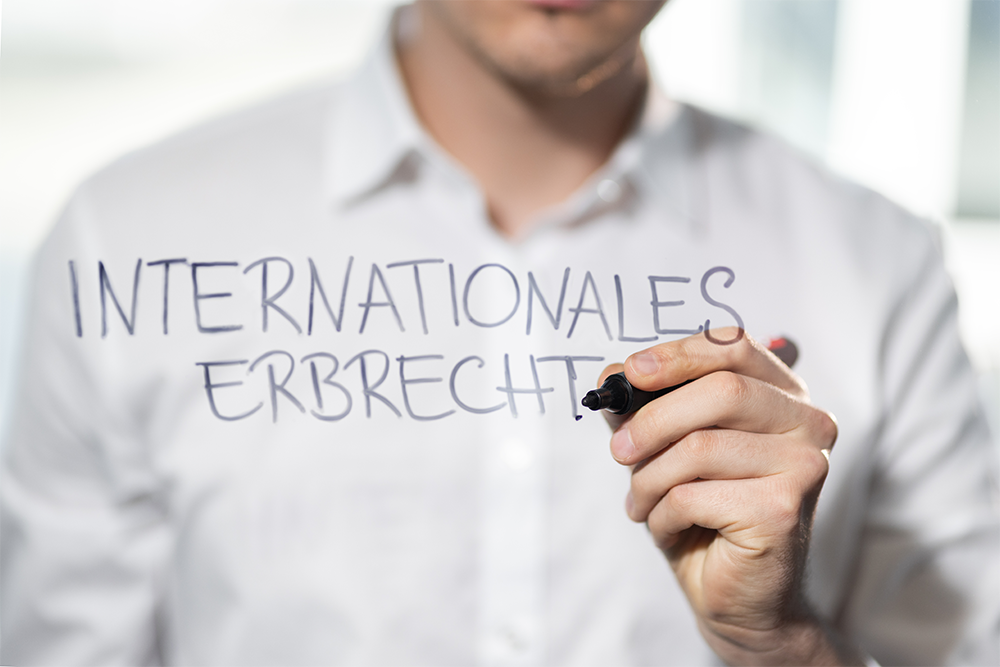 Eine Hand schreibt mit Edding auf eine Glasscheibe "Internationales Erbrecht".