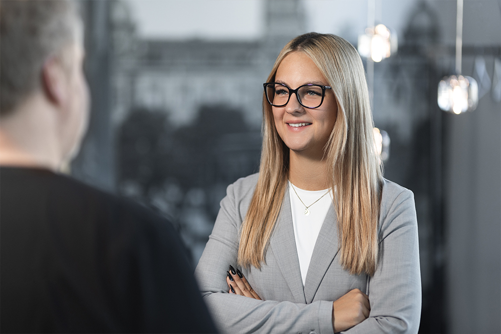 Eine Frau mit Brille spricht mit verschränkten Armen mit einem Mann.